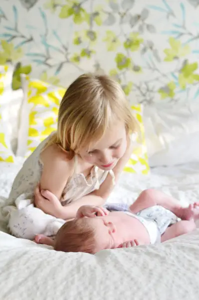 Grote zus kijkt naar baby-broertje bij doe-het-zelf pasgeboren fotoshoot