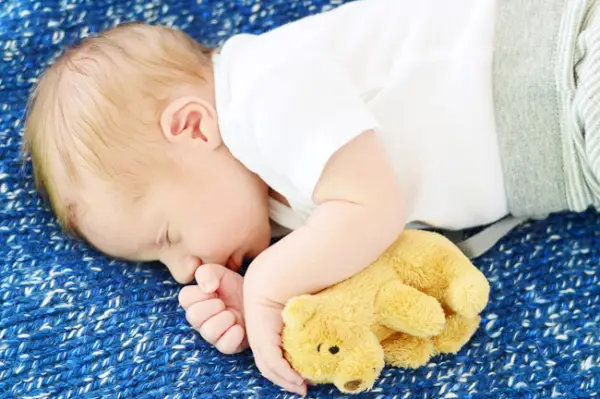 Neugeborenes Foto eines kleinen Sohnes auf einer selbstgemachten Strickdecke und einem kleinen Bären