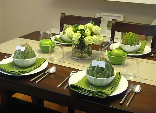 Configuração de mesa com guardanapos verdes e alcachofras como porta-cartões