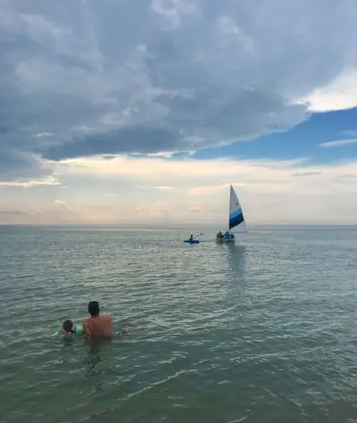 lidé sedí ve vodě a sledují plachetnici na pláži Cape charles