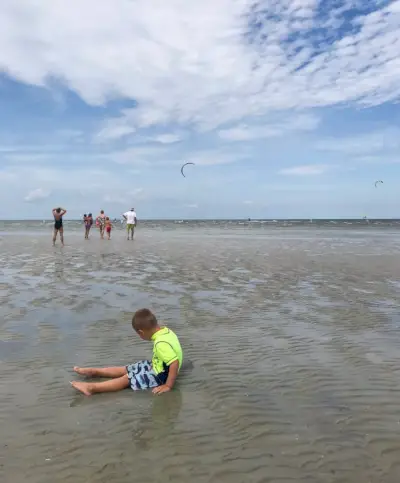 enfant assis dans des eaux peu profondes et avec des kitesurfeurs à la plage de Cape Charles