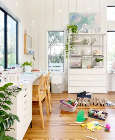 Espaço luminoso para artesanato em sala familiar com mesa e piso coberto com materiais de artesanato e arte