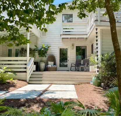 Façade d'une maison moderne blanche avec beaucoup de verdure et une grande passerelle en béton