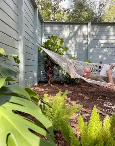 John legger i hengekøye på sidegården blant tropiske planter