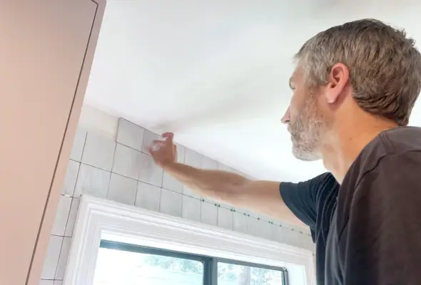 John adicionando a última linha de azulejos acima da janela da cozinha