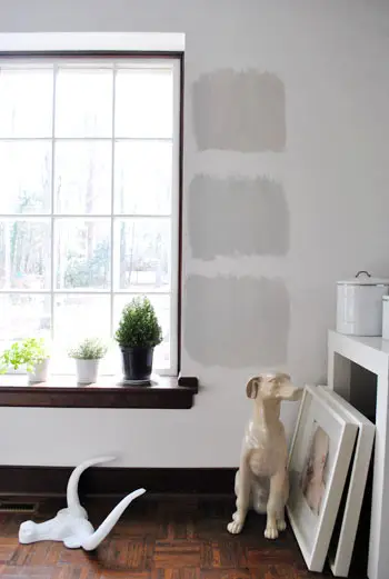 tres opcions de pintura gris Benjamin Moore pintades com a quadrats de prova en una paret blanca amb adorns de fusta