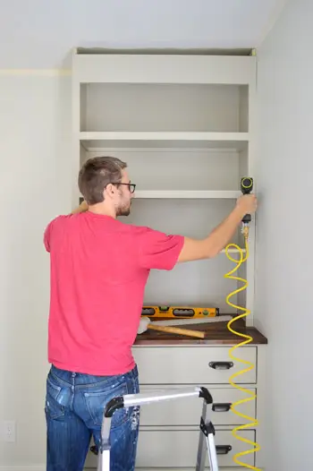 Homme clouant des pièces de garniture sur la face d'une étagère de bricolage