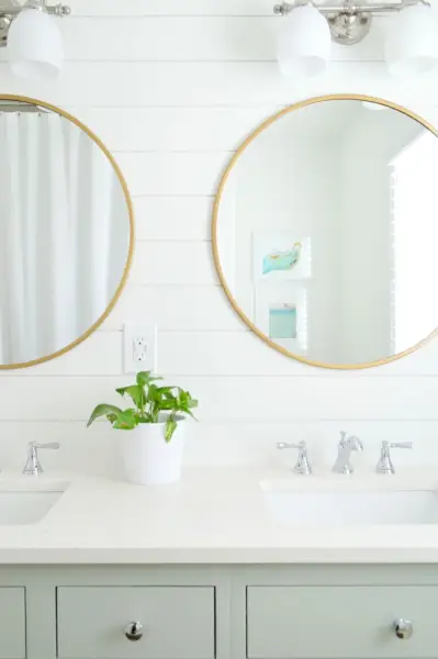 Salle de bain Shiplap avec armoires vertes miroirs ronds dorés murs extra blancs