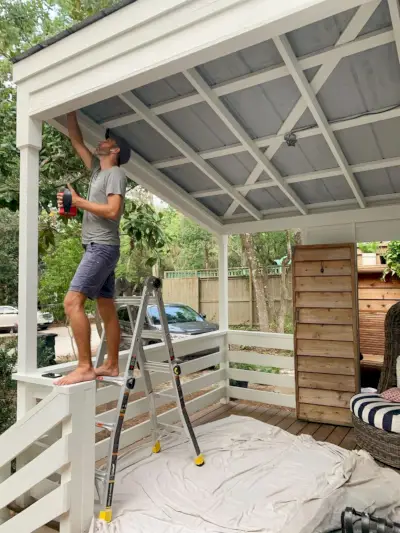 John staat op de ladder en maakt een metalen verandaplafond klaar