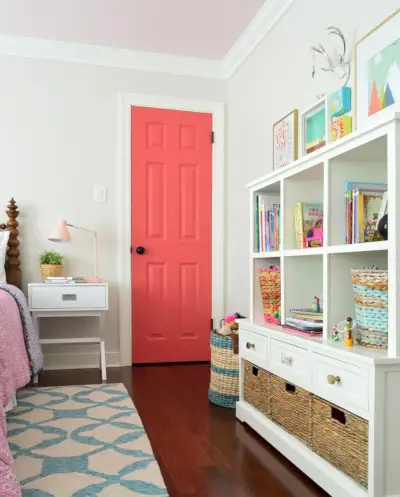 Chambre de filles avec murs grèges, garnitures simplement blanches et porte rose