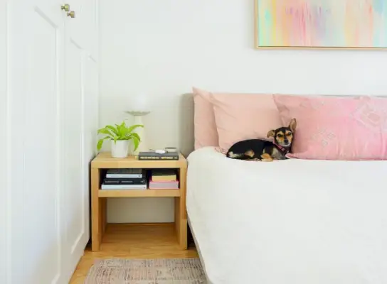 Mesita de noche de madera con bloques de carnicero junto a la cama con Penny The Chorkie durmiendo sobre una almohada rosa