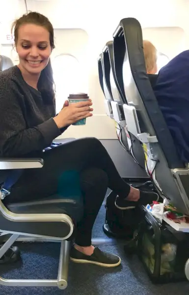 Sherry assise dans un avion avec une cage de transport pour chien sous le siège devant elle